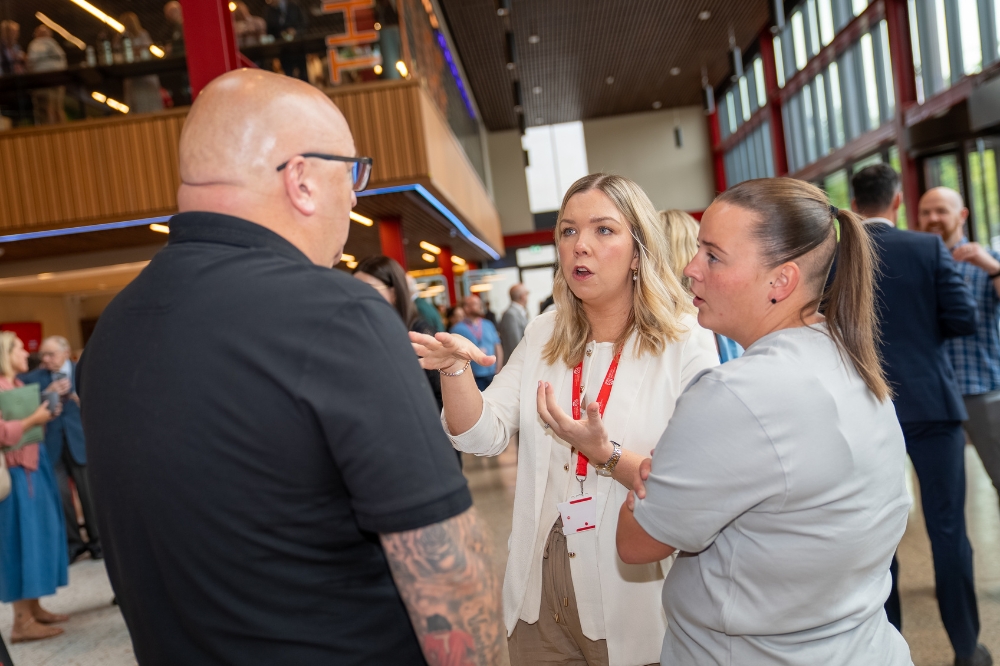 young woman in smart, cream-coloured dress talking with a tattooed man and young woman