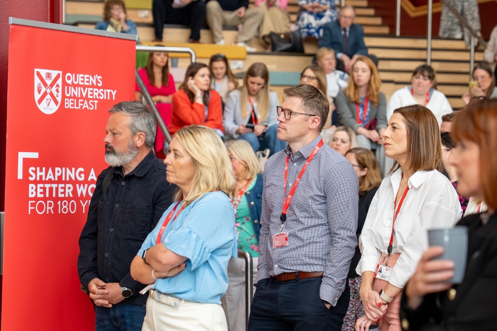 smart group of professional-looking people standing in front of and seated on steps, listening to an address at an indoor event