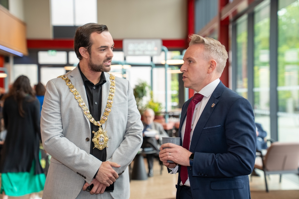 two men, one wearing a mayoral chain, chatting in an airy indoor space