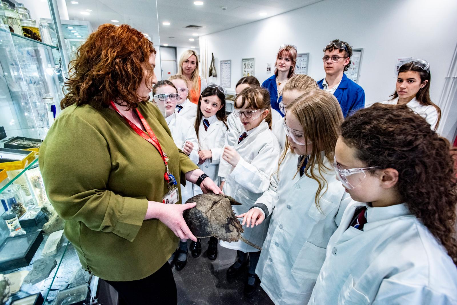 Schoolchildren dressed in lab coats looking at a fossil