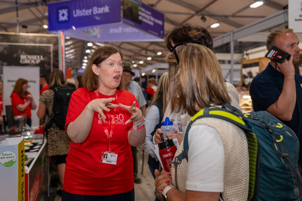 woman in red t-shirt chatting informatively and excitedly to a visitor at an indoor exhibition