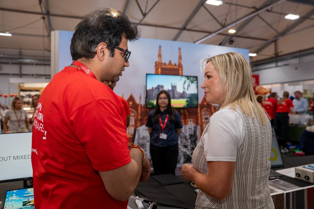 man in red t-shirt talking to a woman with an exhibition stand and female representative in the background