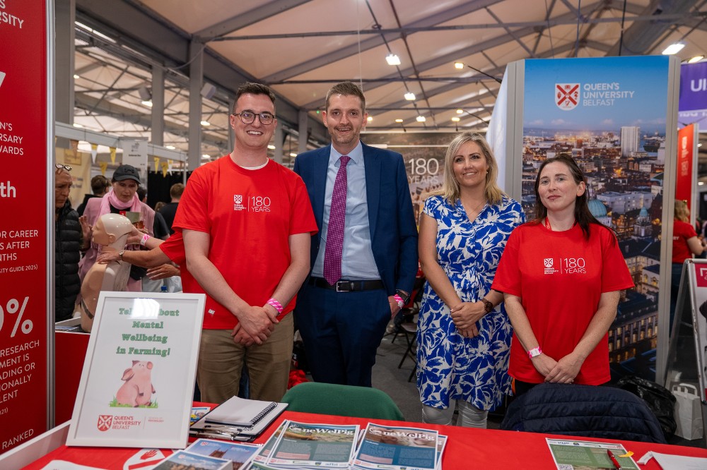Smiling, smartly dressed man and woman flanked by man and woman in red t-shirts at an exhibition stand