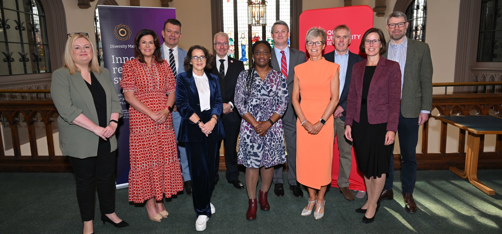group of people smiling to camera on a balcony in an old building with a stained-glass window in the background