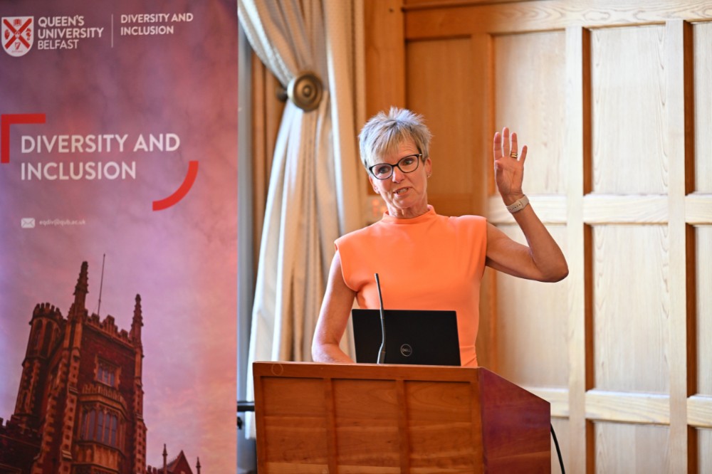 woman in coral-coloured dress talking from a podium in a boardroom setting