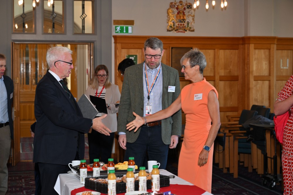 man and woman just about to shake hands over a coffee table with other people in the background