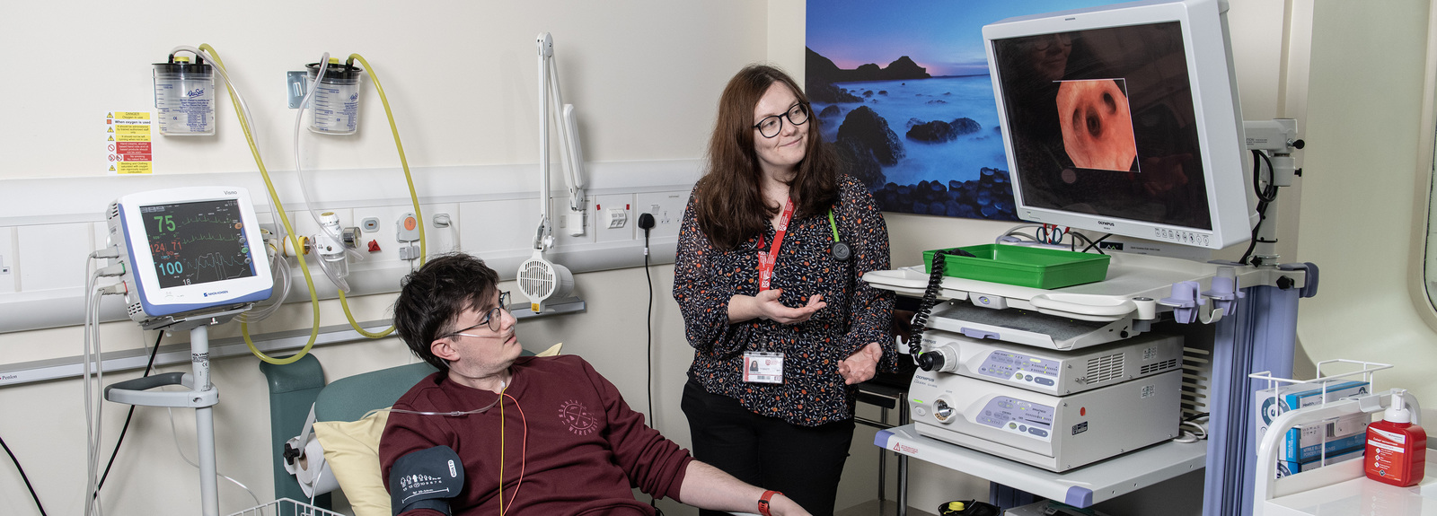Female doctor showing male patient imagery on screen while he lies on hospital bed