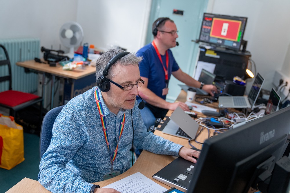 two men working on computers and running AV equipment from a green room