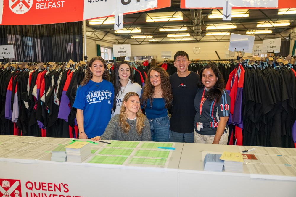 group of five young women and a man manning an indoor gown collection point