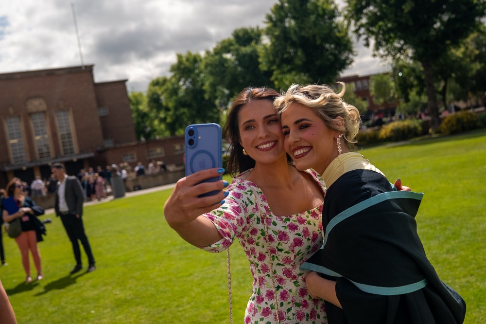two women posing for a selfie on a large lawn in the sunshine