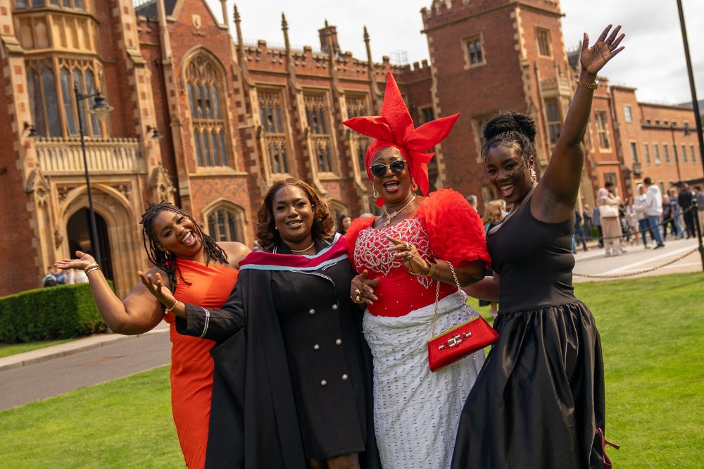 four women of African origin in celebratory pose on a lawn outside a redbrick building