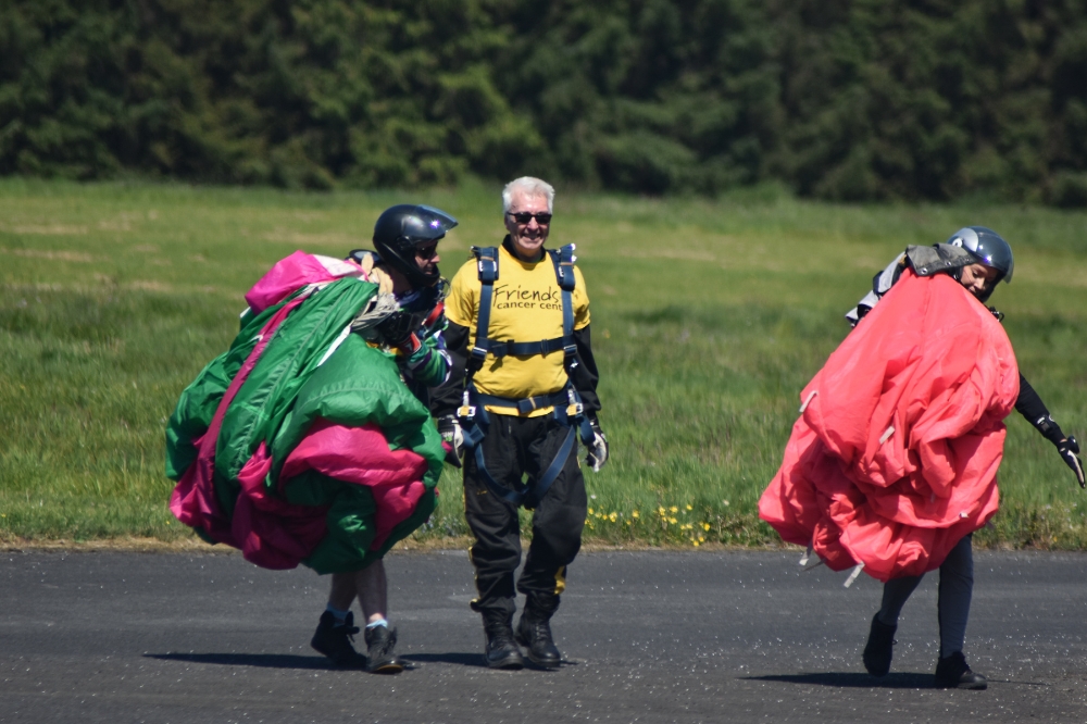 man in yellow charity t-shirt walking on tarmac flanked by two skydiving instructors carrying parachutes