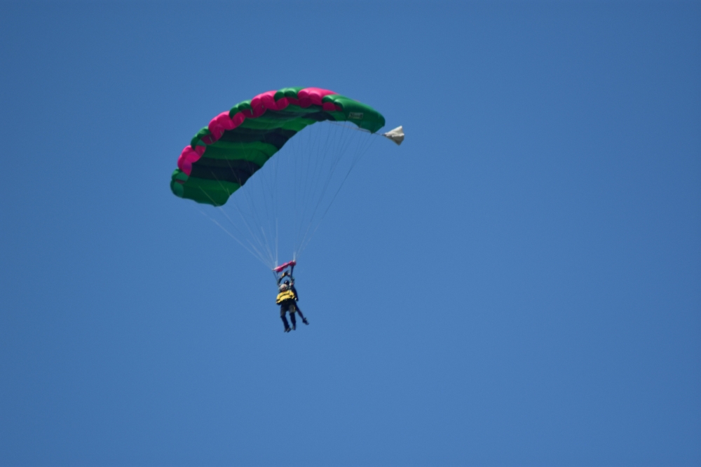 photo taken from the ground of two people completing a tandem skydive with parachute open