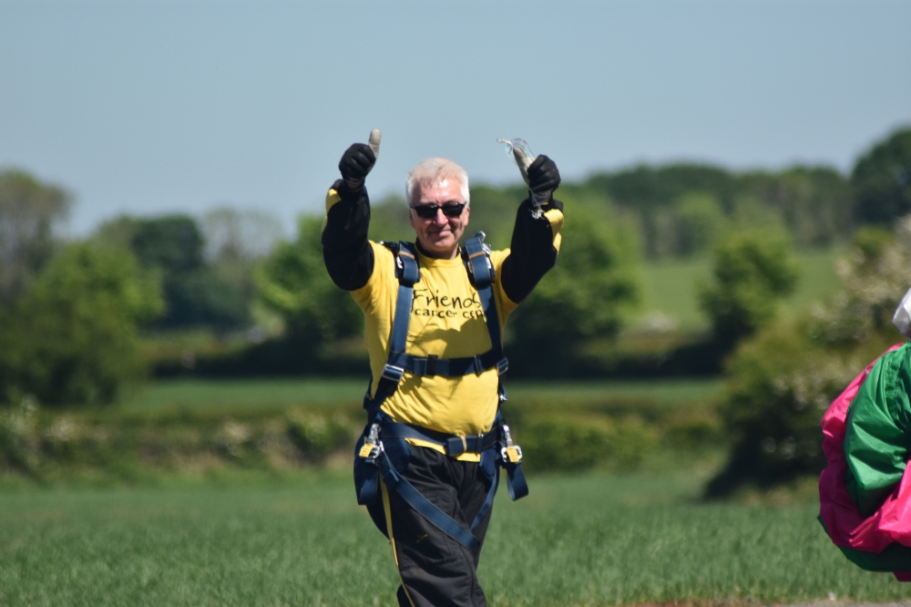 smiling man in yellow charity t-shirt and skydiving harnesses giving two thumbs up