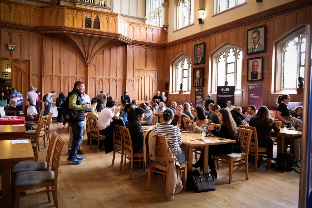 large group of people sitting, standing and enjoying light refreshments in a grand, wood-paneled hall bright sunshine pouring through the windows