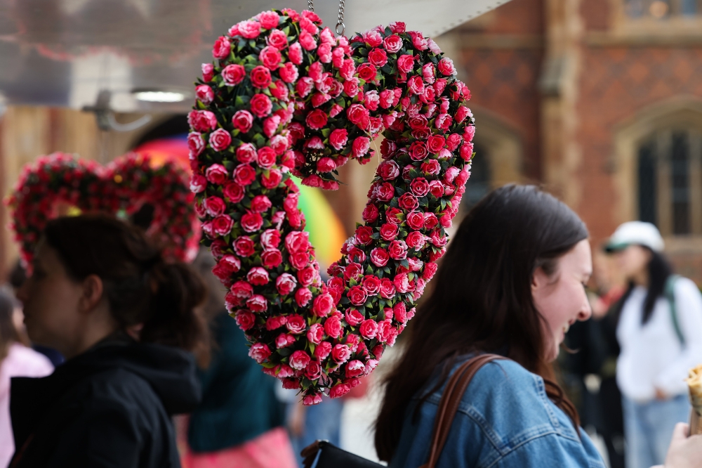 heart-shaped wreath with pink-red flower decorations hanging in an outdoor space with people in the background