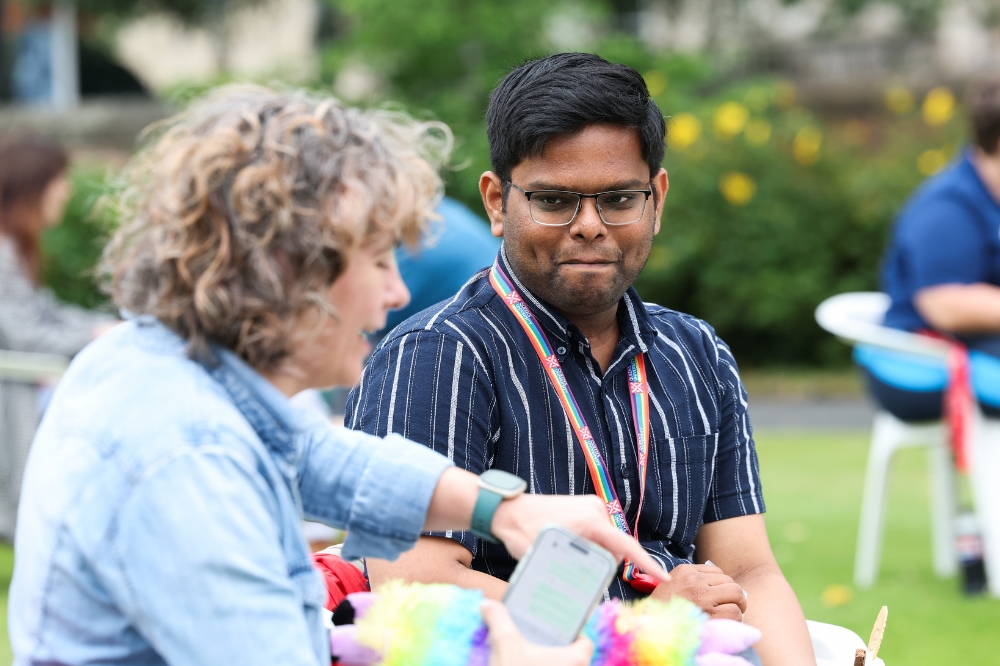 male of Asian origin chatting with a female acquaintance at a seated outdoor event
