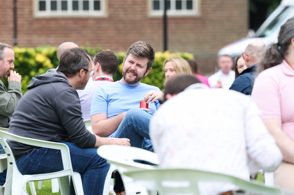 two men chatting at an outdoor seated event with other out-of-focus people in the foreground and background