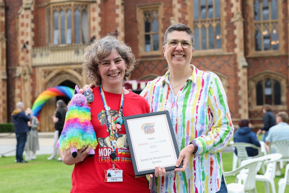two smiling women, one presenting the other with a framed certificate - the other is holding a rainbow llama piñata