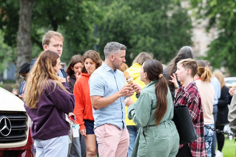 group of people chatting at an outdoor event with trees shown in the background