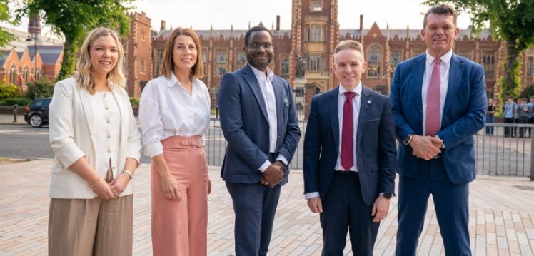 Two women and three men stand outside a historic university building on a sunny day looking at the camera