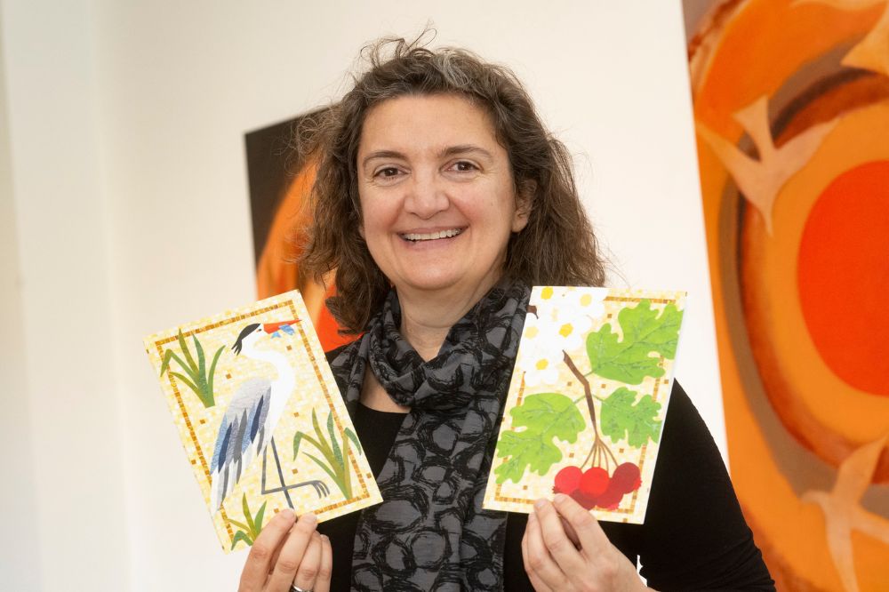 A smiling lady holding two art pieces at Reach'25