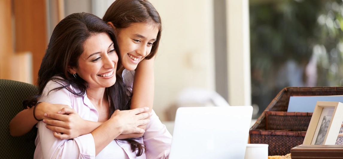 A mother and daughter sharing a warm hug while sitting together with a laptop.