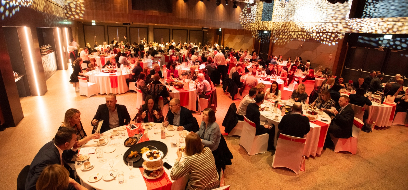 large group of smartly dressed people seated at dinner tables in a warmly-lit event space