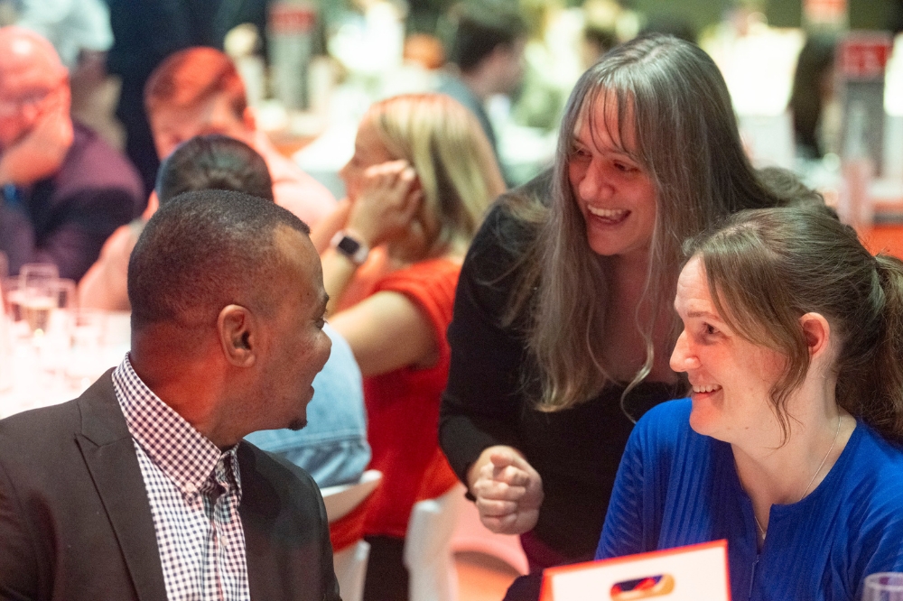smiling woman stopping at a table to talk to a friend at a gala event
