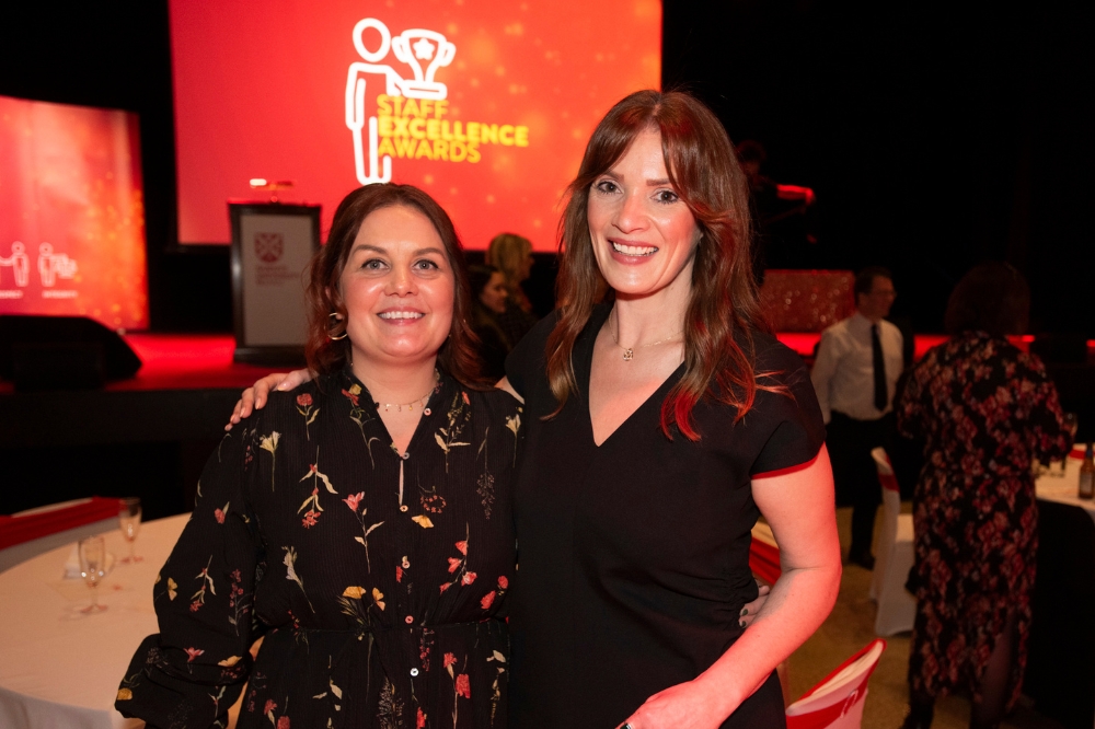two women smiling for the camera. Background screen graphic reads 'Staff Excellence Awards'.