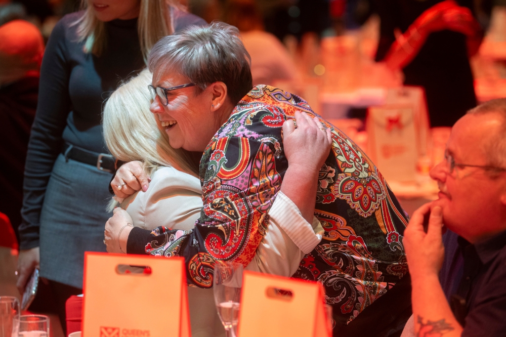 woman hugging another woman at a dinner table at a gala event