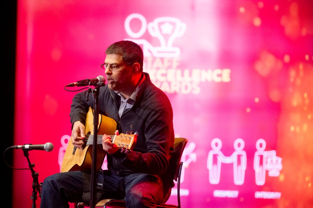 seated man playing guitar and singing on stage at a gala event