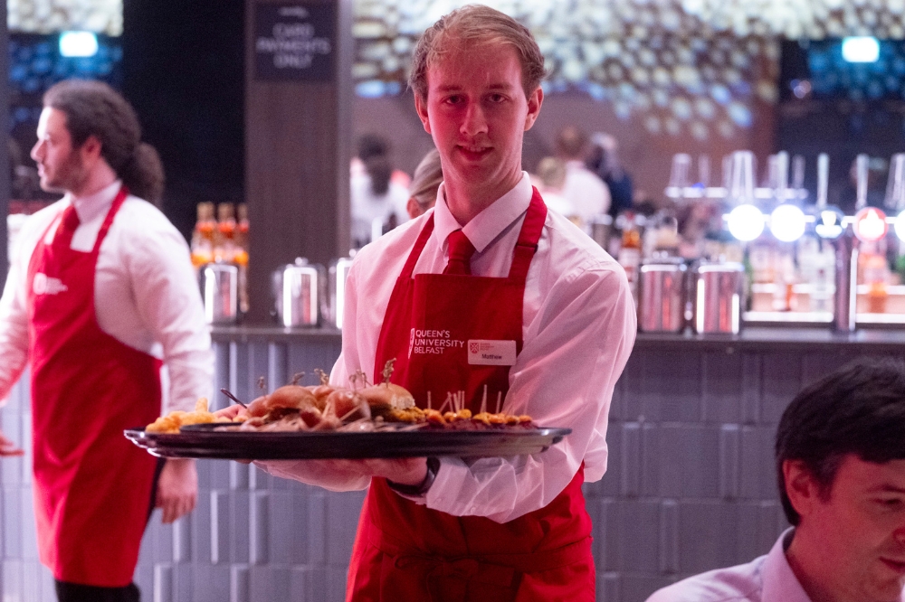 young man in white catering shirt and red apron serving food at an event