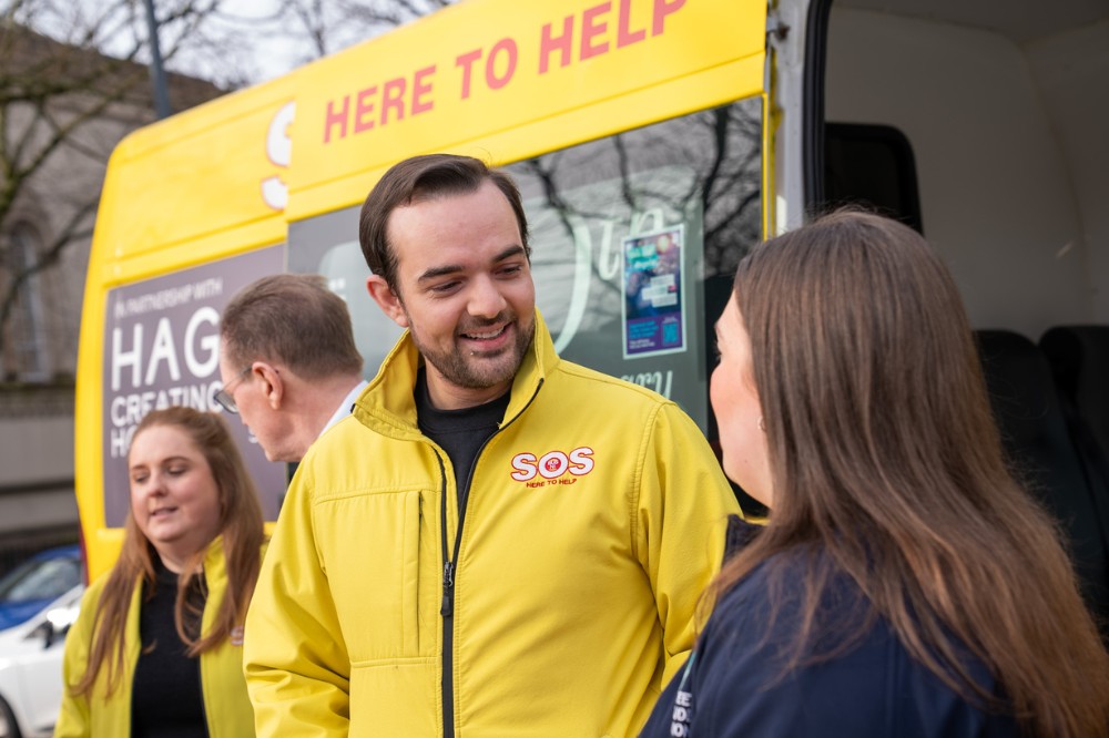 four people chatting in front of a yellow minibus