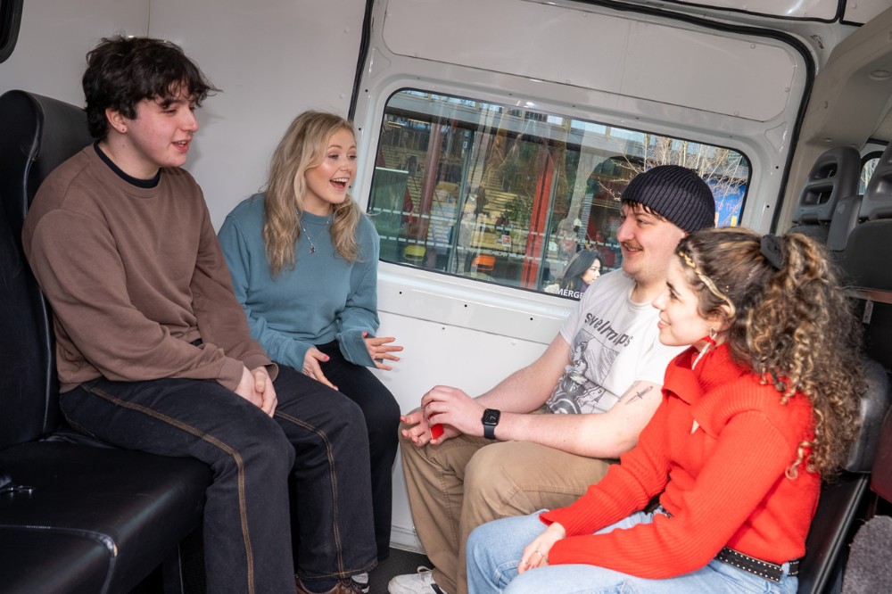 four young people - two men, two women - chatting in a friendly manner in a minibus