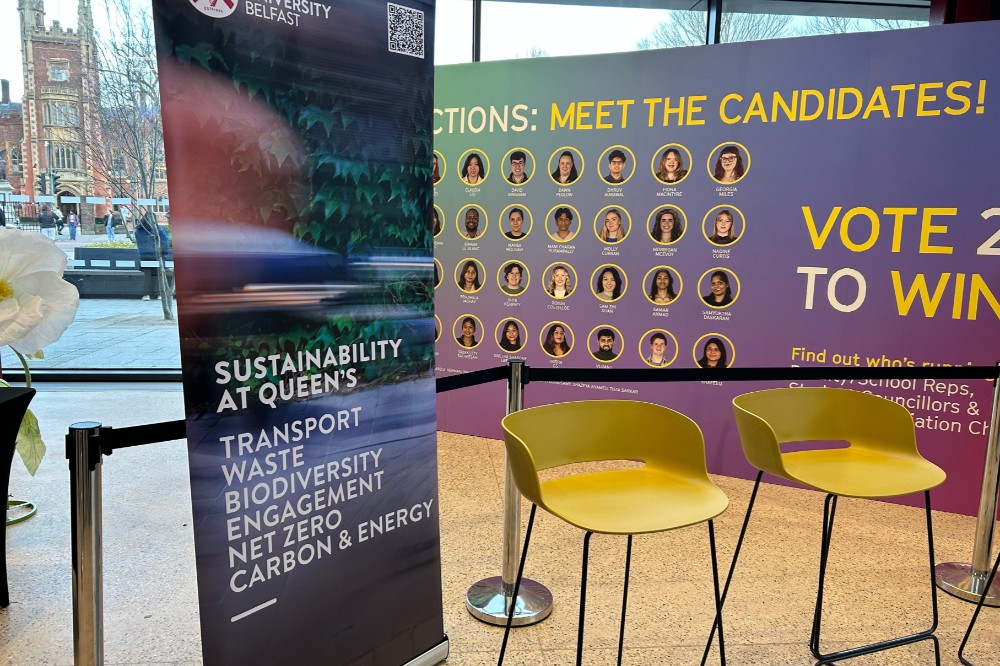 a pop-up banner displaying sustainability-related words and a set of high stools standing in front of a larger banner showing candidates for an election