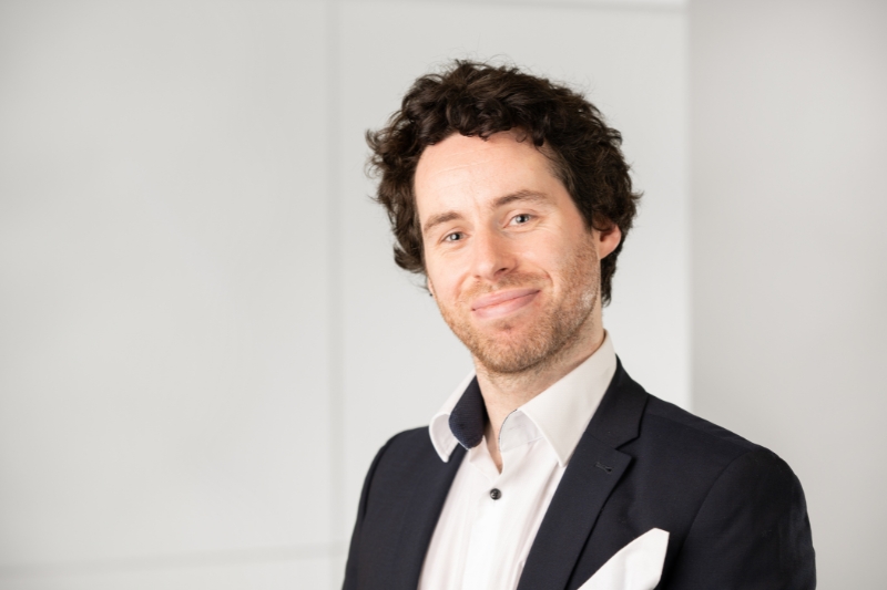 Headshot of a dark curly haired man wearing a white dress shirt and black blazer with a white handkerchief